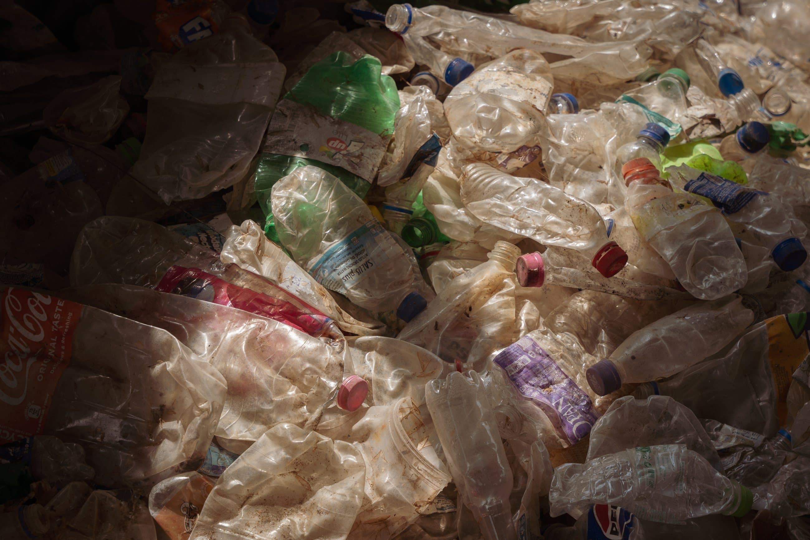 Flattened recovered plastic bottles in warm low light, ready for baling.