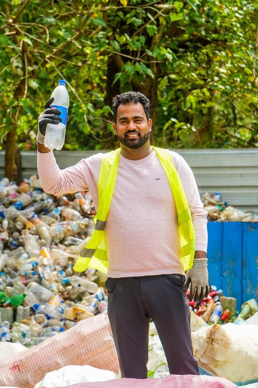 An NRC collector in a high-visibility vest holding up a recovered bottle in front of masses of collected plastic bottles.